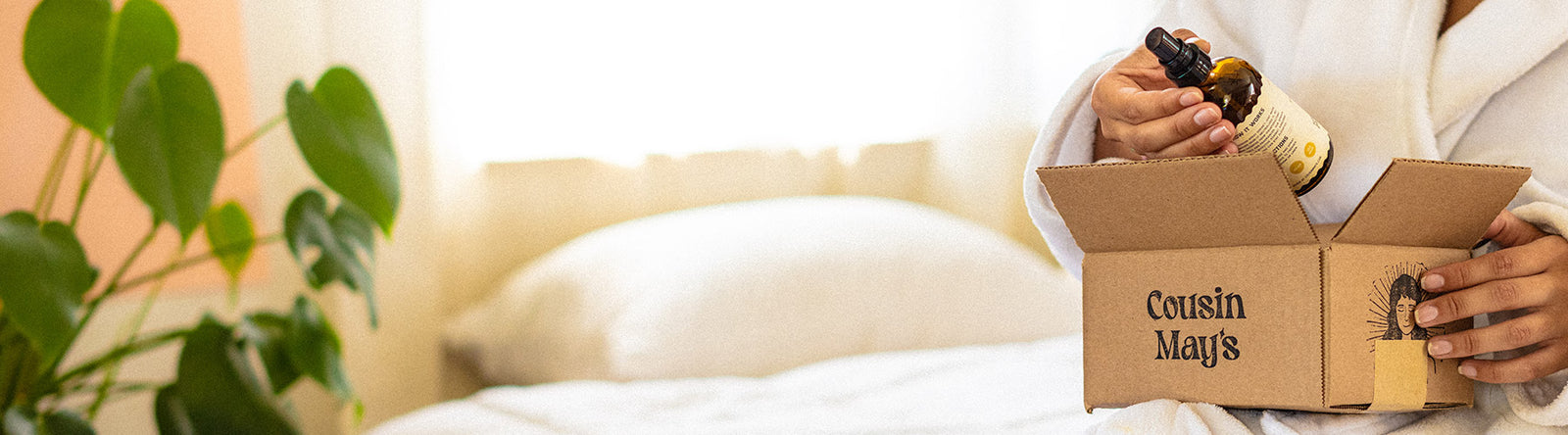 A robed woman sits in bed and unboxes a beautiful package from Cousin May's.